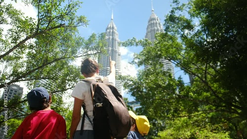 Fearless single mother travels with her 5 and 7-year-old children, exploring Kuala Lumpur's Petronas Towers and Southeast Asian cityscape on a summer adventure, proving that family travel knows no bou photo