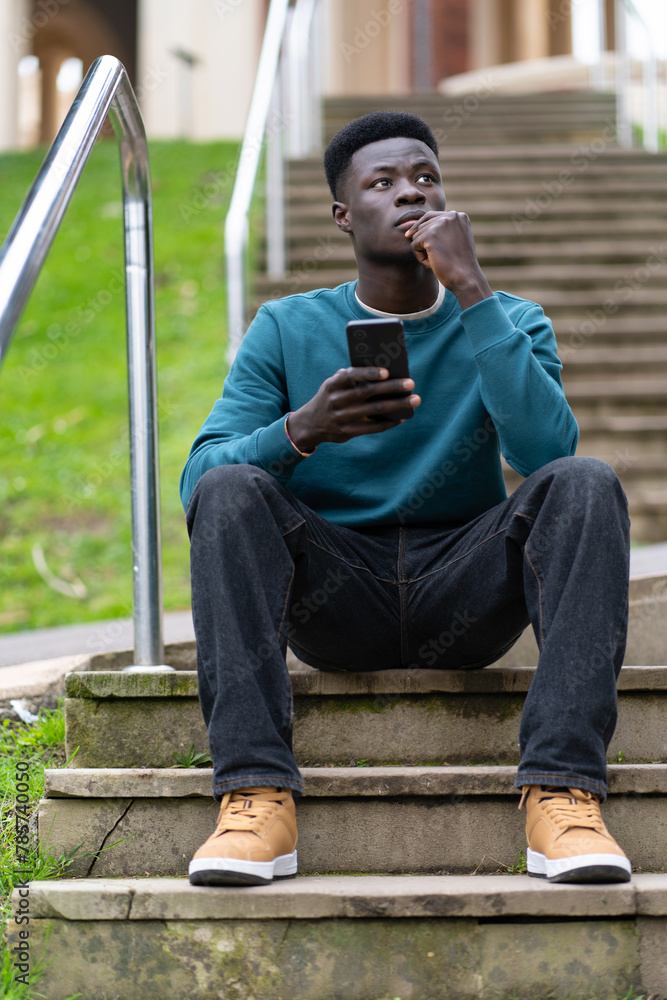 A young man sits on a set of stairs with his cell phone in his hand