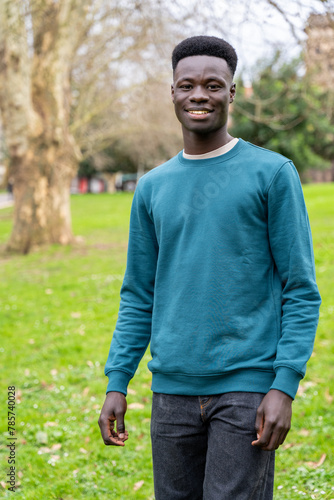 A young man wearing a blue sweater stands in a grassy field