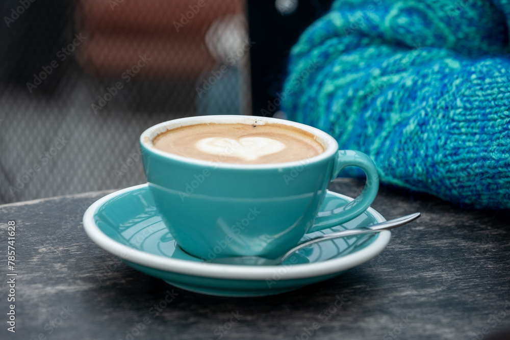 Cozy cappuccino with heart shaped foam in a teal cup, accompanied by a knit sweater, evoking warmth and comfort. Cozy cappuccino with heart shaped foam in a teal cup, accompanied by a knit sweater, evoking warmth and comfort.