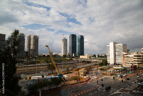  Urban skyline of Ramat Gan, Israel, under dramatic clouds, showcasing modern high-rises, construction, roads, and greenery