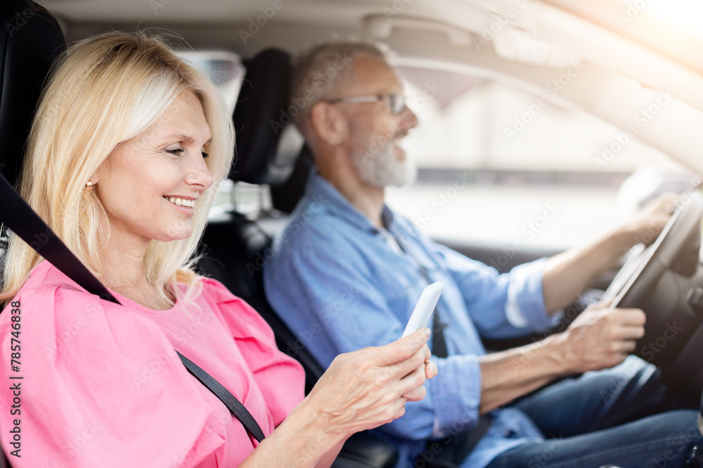 Obraz premium Smiling senior woman using phone, man drives in car