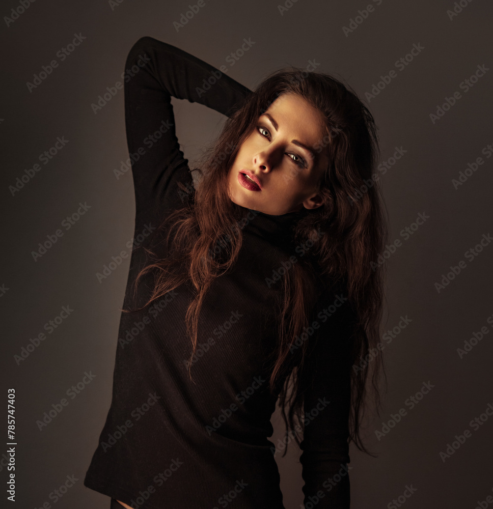 Beautiful makeup sexy woman with red lipstick in black poloneck posing on dark shadow studio black background. Long brown volume hairstyle. Closeup Beautiful makeup sexy woman with red lipstick in black poloneck posing on dark shadow studio black background. Long brown volume hairstyle. Closeup