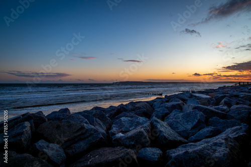 Evening sunset over Camber sands in East Sussex, Image shows a the end of a beautiful golden orange sunset over the beach and coastal defence rocks with a receding tide reflecting the evening colours photo