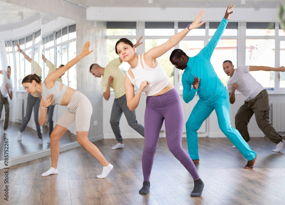 Fototapeta premium Expressive young Asian woman honing hip-hop dance moves in mirrored choreographic studio setting during group training..