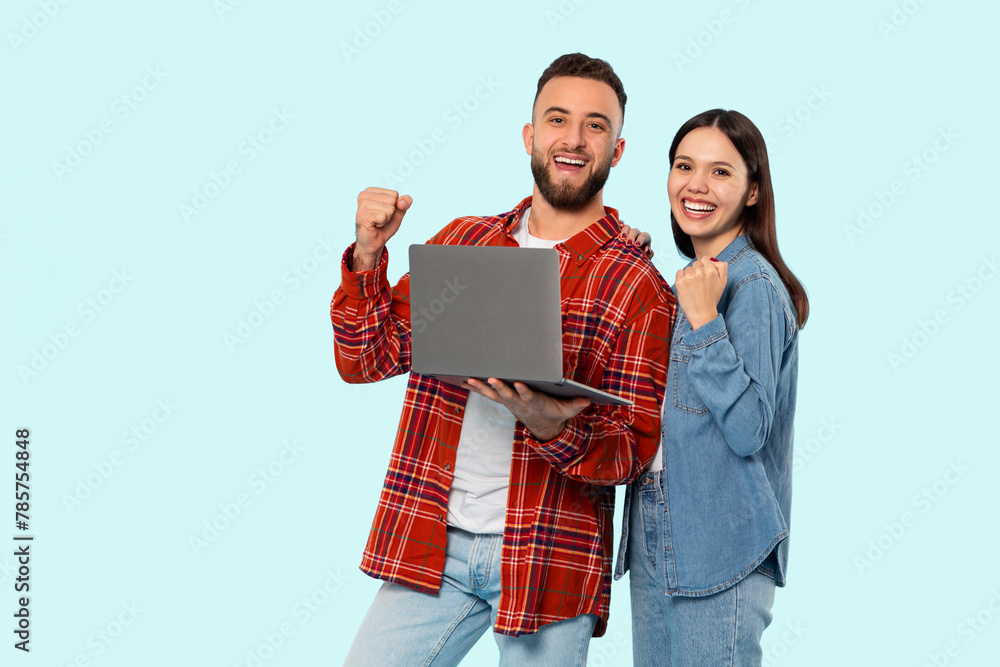 Happy couple with laptop celebrating on blue background