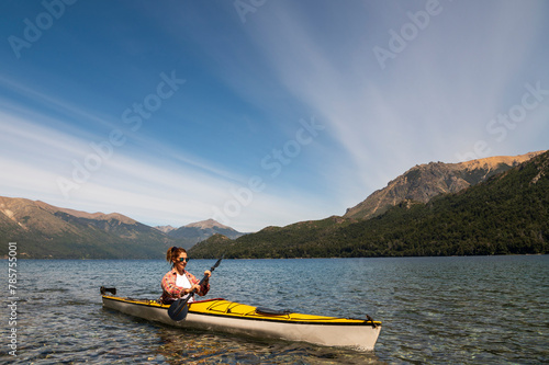 Woman enjoys the scenery of the lake and mountains while sightseeing kayaking on the lakes of Bariloche in Patagonia Argentina during her vacation.