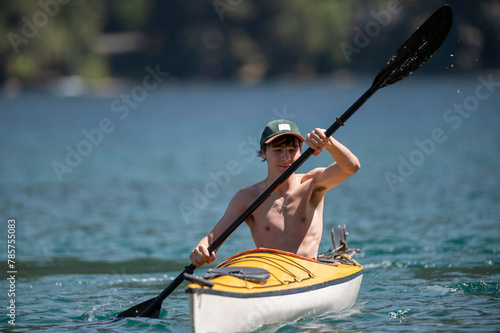 Young happy teenager paddles a kayak through the lakes of the Nahuel Huapi National Park, surrounded by mountains and forests. Patagonia, Argentina. photo