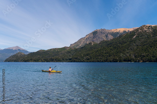 Young happy teenager paddles a kayak through the lakes of the Nahuel Huapi National Park, surrounded by mountains and forests. Patagonia, Argentina.