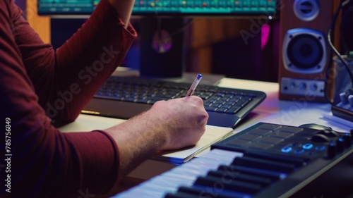Composer developing an original track In his home studio, writing down lyrics and harmonic notes before recording the song melody. Musician using DAW computer apps for creating music. Camera A.