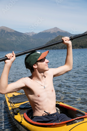 Teenager enjoys kayaking and sunbathing with his arms raised while paddling through the lakes of Bariloche during his summer vacation. Argentina, Patagonia.