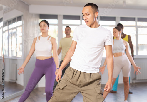 European guy teaches sequences of movements, actions during dance lesson, trains to doing elements of dancehall dance, enjoys active hobby. Multinational group rehearsal, dance choreography coach