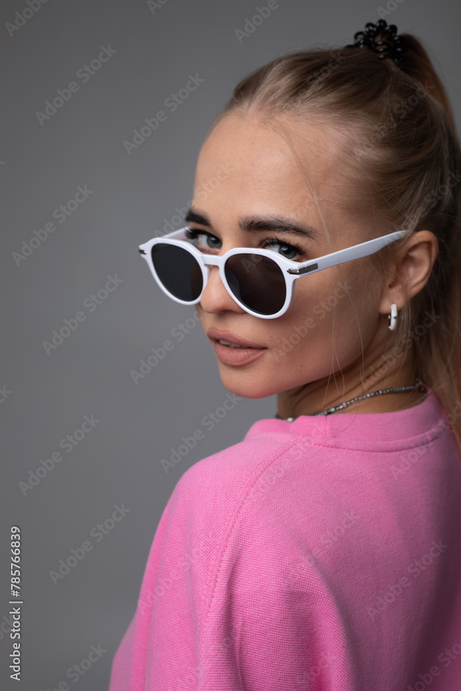Beautiful blonde woman in sunglasses, pink hoodie and white panties posing on gray background Beautiful blonde woman in sunglasses, pink hoodie and white panties posing on gray background