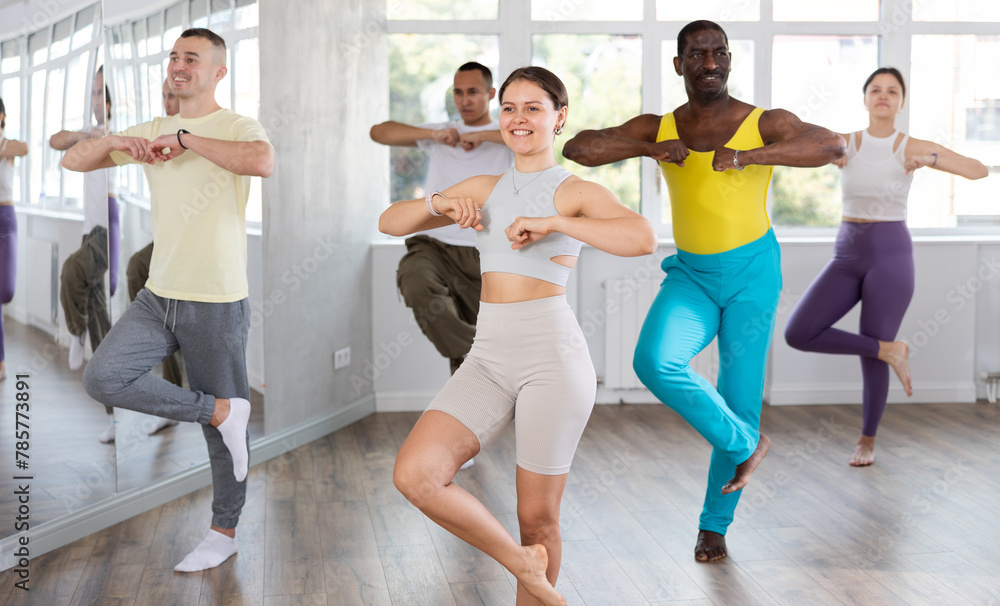 Obraz premium Emotional attractive young girl learning movements of traditional Caucasian dance lezginka during group training for adults in modern dance hall