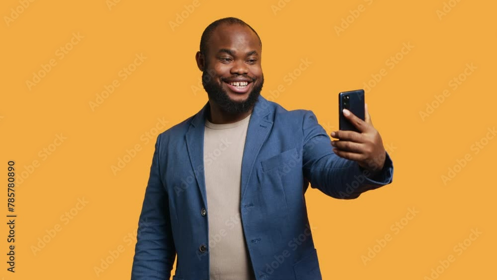 Joyous man using smartphone to take selfies and post them on social media. Happy BIPOC person taking photos using phone selfie camera, isolated over yellow studio background, camera A Joyous man using smartphone to take selfies and post them on social media. Happy BIPOC person taking photos using phone selfie camera, isolated over yellow studio background, camera A