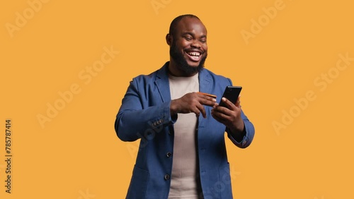 Happy man adding payment method on phone website, delighted to take advantage of promotions, studio background. Person thrilled to do internet shopping, typing credit card data on smartphone, camera B photo