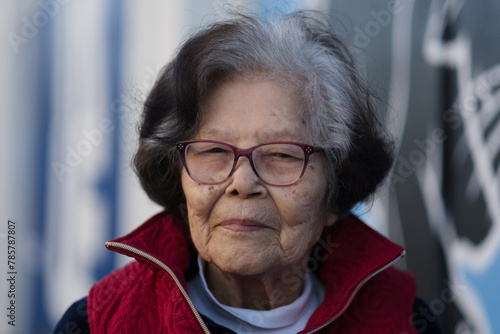 A woman in her nineties poses for a portrait outdoors. She looks at the calm with a gentle, content expression. She is Asian, of Okinawan (Ryukyuan) descent.