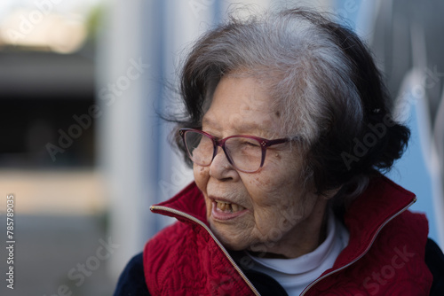 An elder grandmother over ninety years old turns to the side, mid-conversation, in a candid photo while sitting outdoors. She is from Okinawa (she is Ryukyuan), a blue zone with high longevity.
