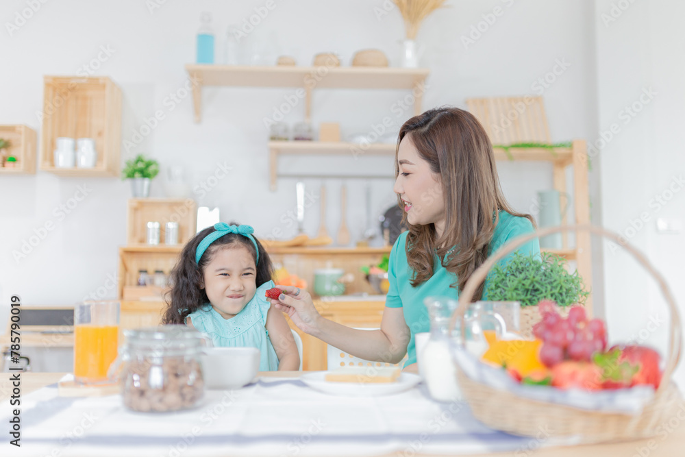 Asian children and her mom have a breakfast in the morning, they eating a fresh organic strawberries, child nutrition and development, they feeling happy in family time