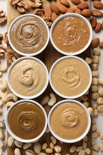 Many tasty nut butters in bowls and nuts on white table, flat lay