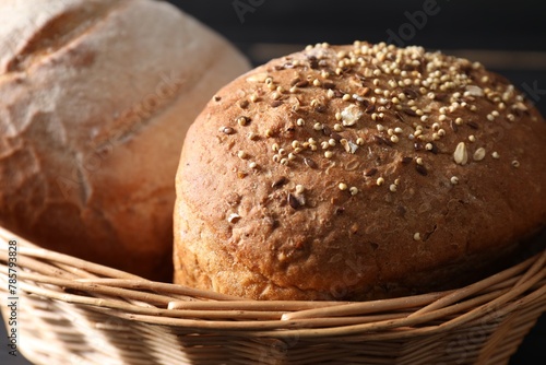 Wicker basket with fresh bread on dark background, closeup photo