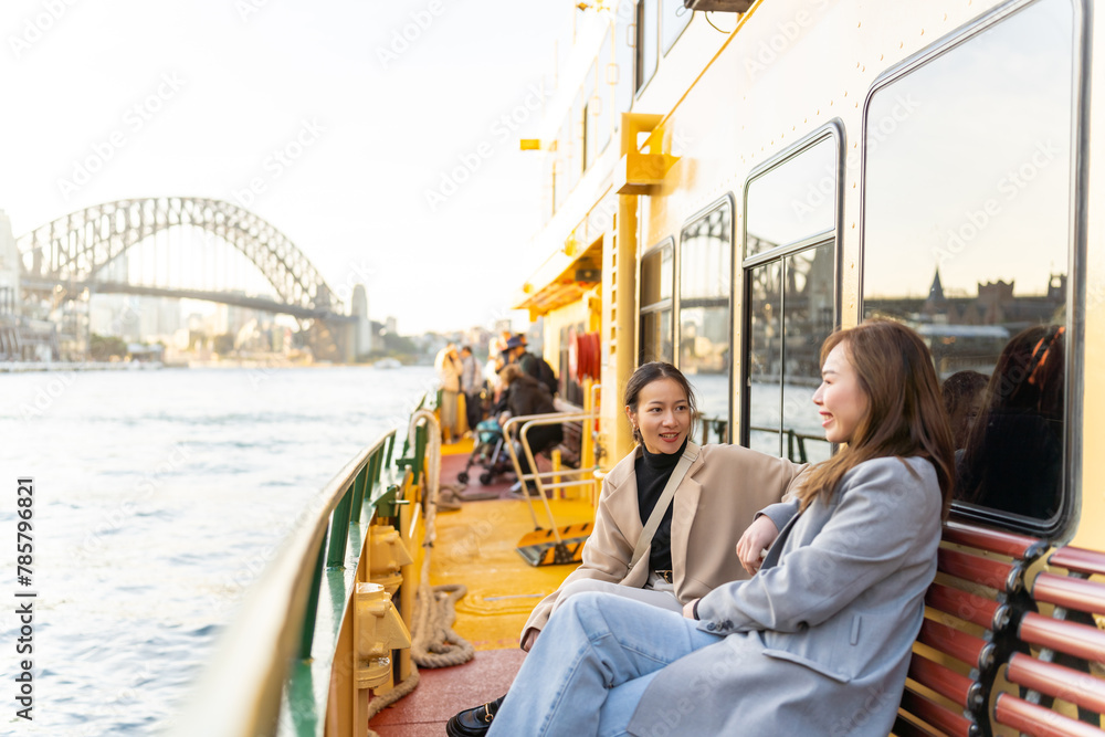 Fototapeta premium Happy Asian woman friends sitting on ferry boat crossing Sydney harbour in Australia. Attractive girl enjoy and fun urban outdoor lifestyle shopping and travel in the city on holiday vacation.