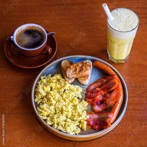 Full breakfast with scrambled eggs, toast, sausages, coffee, and a smoothie on a wooden table