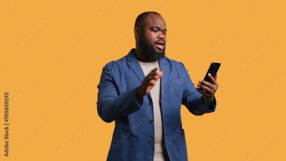 Upbeat man having friendly conversation with friends during teleconference meeting using smartphone, studio background. BIPOC person has fun catching up with mates during online videocall, camera B Upbeat man having friendly conversation with friends during teleconference meeting using smartphone, studio background. BIPOC person has fun catching up with mates during online videocall, camera B