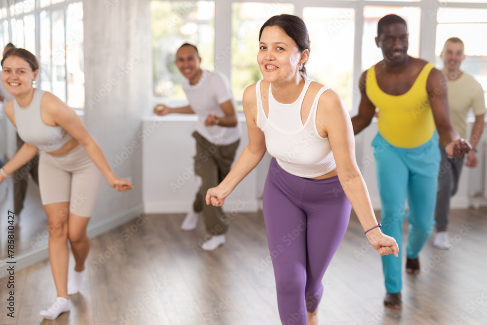 Fototapeta premium Asian woman conducts lesson for multinational people company, teaches men and woman to move aesthetically to beat of music, control their bodies and perform modern energy pair dance
