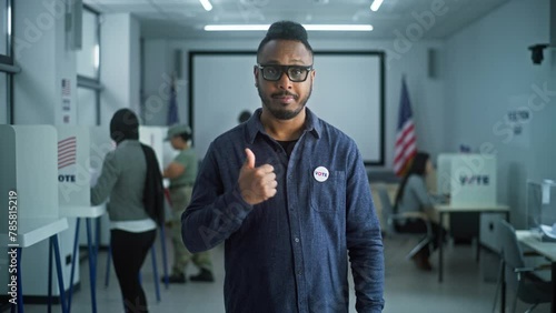 Portrait of African American man, United States of America elections voter. Man with badge stands in modern polling station, poses, looks at camera. Background with voting booths. Election Day in USA. photo