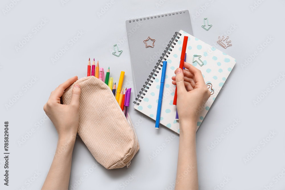 Child's hands with pencil case, different school stationery and notebooks on grey background Child's hands with pencil case, different school stationery and notebooks on grey background