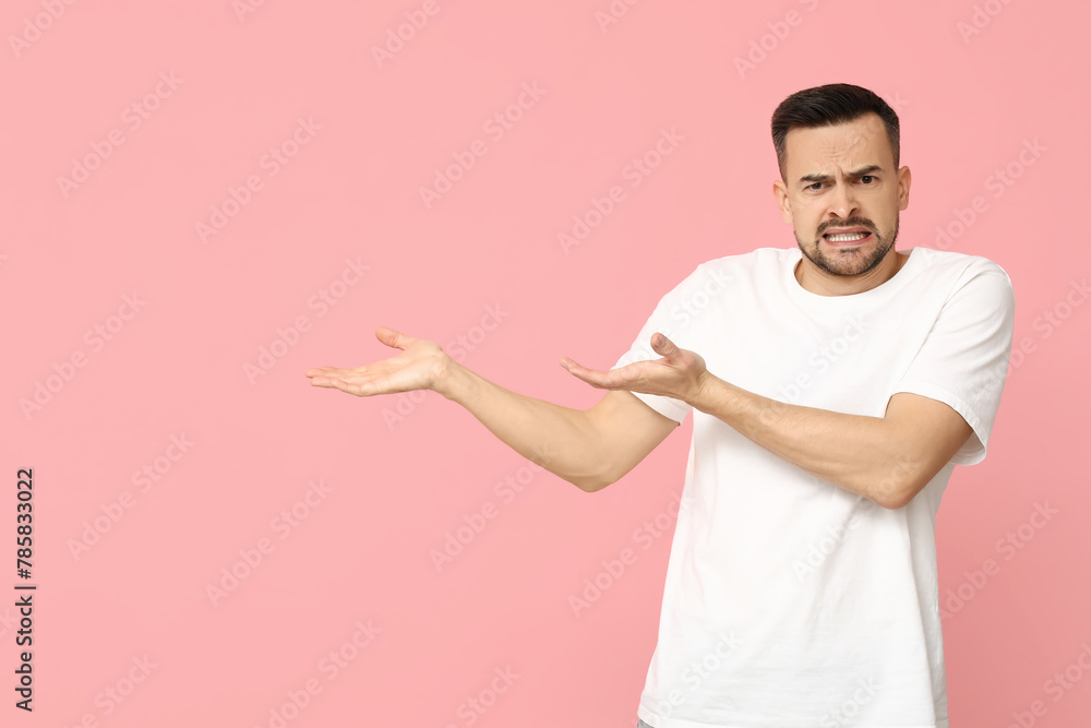 Handsome worried young man showing something on pink background Handsome worried young man showing something on pink background