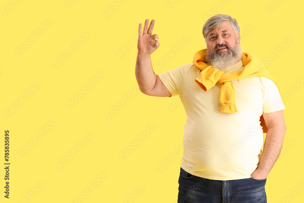 Mature bearded man showing OK on yellow background