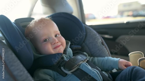 the one year oldgold hair boy is sitting in the car seat, looking out the window, smiling, traveling photo