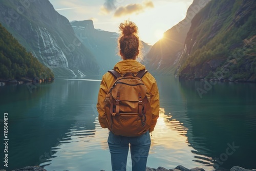 A solo traveler gazes at a serene fjord during sunset, the light reflecting on calm waters.