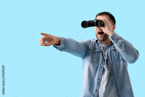 Foto Surprised young man looking through binoculars and pointing at something on blue