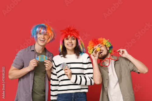 Young friends in funny disguise with paper fishes on red background. April fool s day celebration