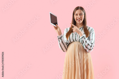 Young pregnant businesswoman pointing at tablet computer on pink background