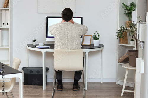 Young businessman suffering from neck pain at table in office, back view © Pixel-Shot