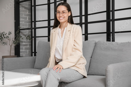 Young beautiful businesswoman sitting on sofa in light office