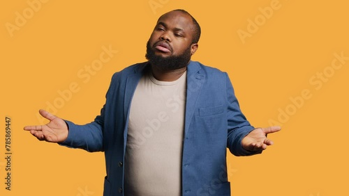 African american man shrugging shoulders, not caring, having detached apathy facial expression. Apathetic BIPOC person doing disinterest indifferent hand gesturing, studio background, camera A