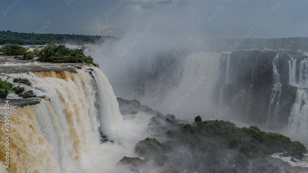 An impressive waterfall landscape. Streams of white foaming water collapse from the edge of the cliff into the abyss. Splashes, fog. Green vegetation on the rocks. Iguazu Falls. Brazil. An impressive waterfall landscape. Streams of white foaming water collapse from the edge of the cliff into the abyss. Splashes, fog. Green vegetation on the rocks. Iguazu Falls. Brazil.