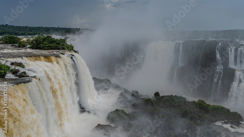 An impressive waterfall landscape. Streams of white foaming water collapse from the edge of the cliff into the abyss. Splashes, fog. Green vegetation on the rocks. Iguazu Falls. Brazil.