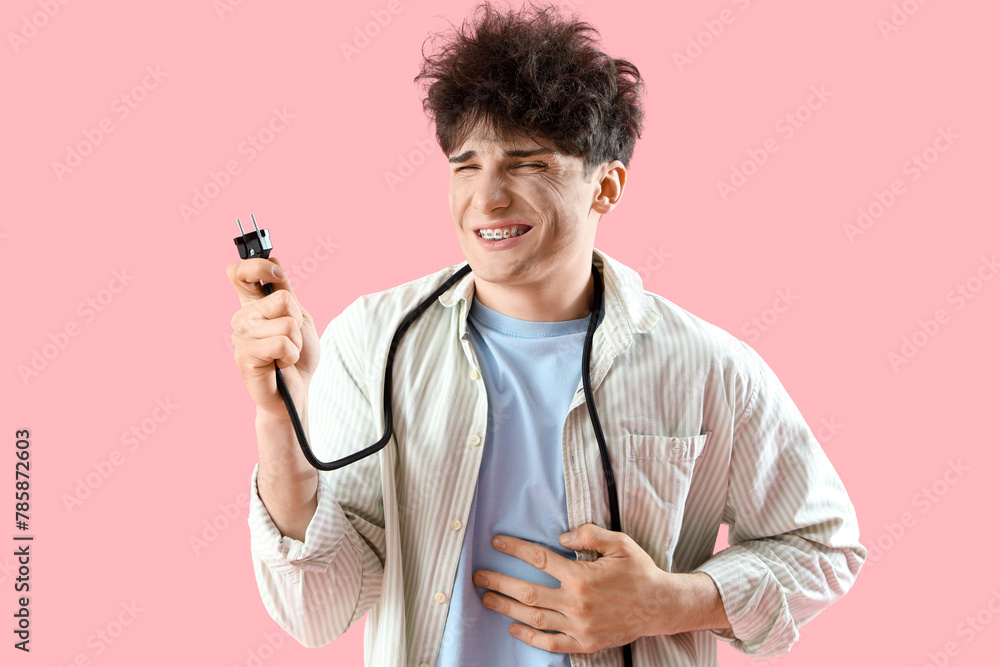 Electrocuted young man with burnt face and plug on pink background Electrocuted young man with burnt face and plug on pink background