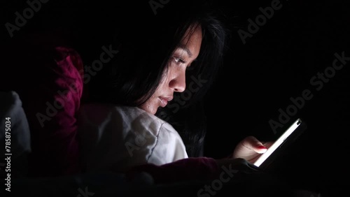 A young woman is lying in bed and using a smart phone