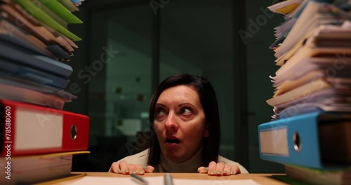 Stressed woman at work at night looking at stack of documents