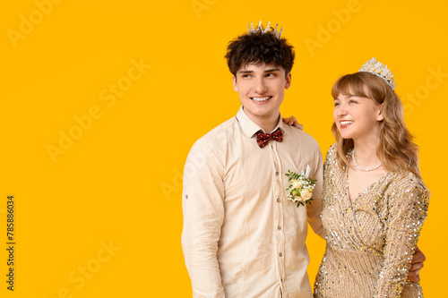 Happy prom couple in crowns on yellow background