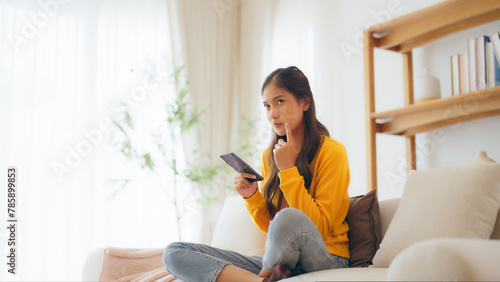 Happy young asian woman relax on comfortable couch at home, typing chat message on smartphone, smiling girl use cell phone chatting, searching information on browser wireless internet, online shopping © Monster Ztudio