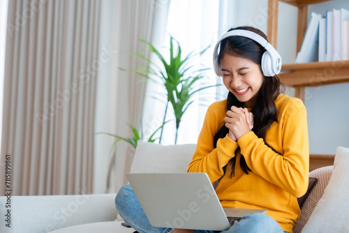Young happy lucky woman student feeling excited winning, using computer laptop and sitting on sofa, adorable Asian female receiving great news on notebook, getting new job celebrating success © Monster Ztudio
