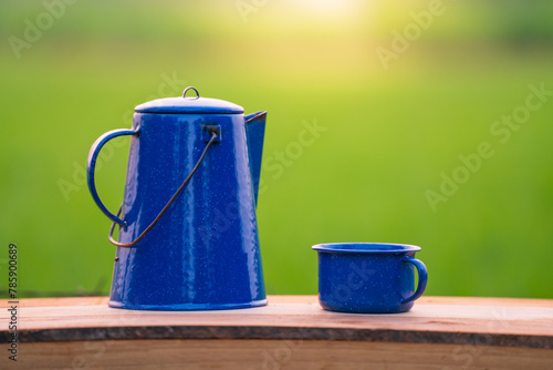 Kettle, blue enamel, and coffee mugs On an old wooden floor, Blurred background of rice fields at sunrise.